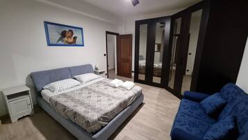 Una camera da letto con un letto, un comodino, un divano blu e una porta che dà su un'altra stanza.