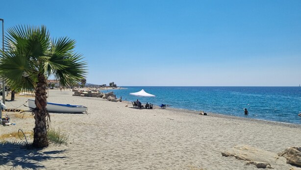 Ein sandiger Strand mit einer Palme, einem weißen Zelt und einem Boot.