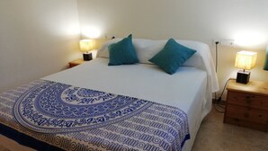 Una cama bien hecha con una colcha estampada, dos almohadas y lámparas de noche sobre mesitas de madera.