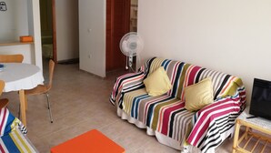 Una sala de estar con un sofá a rayas, un ventilador, una mesa con sillas y un televisor sobre un mueble.