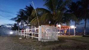 A fenced outdoor area with a hammock and string lights, surrounded by palm trees.