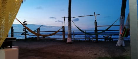 A beach view with a hammock, wooden fence, and a signpost.