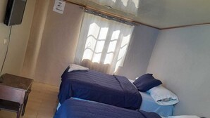 A room with two beds, a small table, and a window with curtains.
