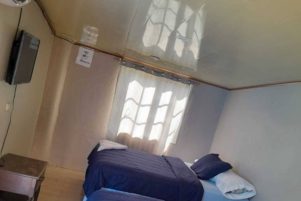 Una habitación con dos camas, una mesita y un ventanal con cortinas.