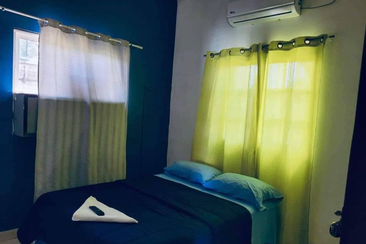 Un dormitorio con cama, ventana con cortinas estampadas y un equipo de aire acondicionado.
