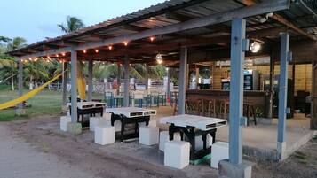 An outdoor seating area with tables and chairs, a covered shelter, and a bar area with stools.
