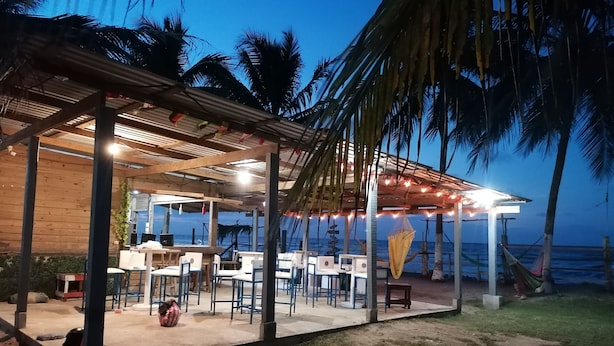 An outdoor seating area with tables and chairs, a covered section with string lights, and a view of the ocean.