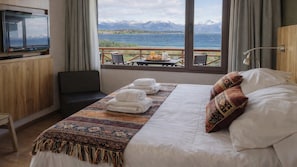 Een hotelkamer met een bed, een televisie, uitzicht op bergen en een meer, en een ontbijttafel met eten.