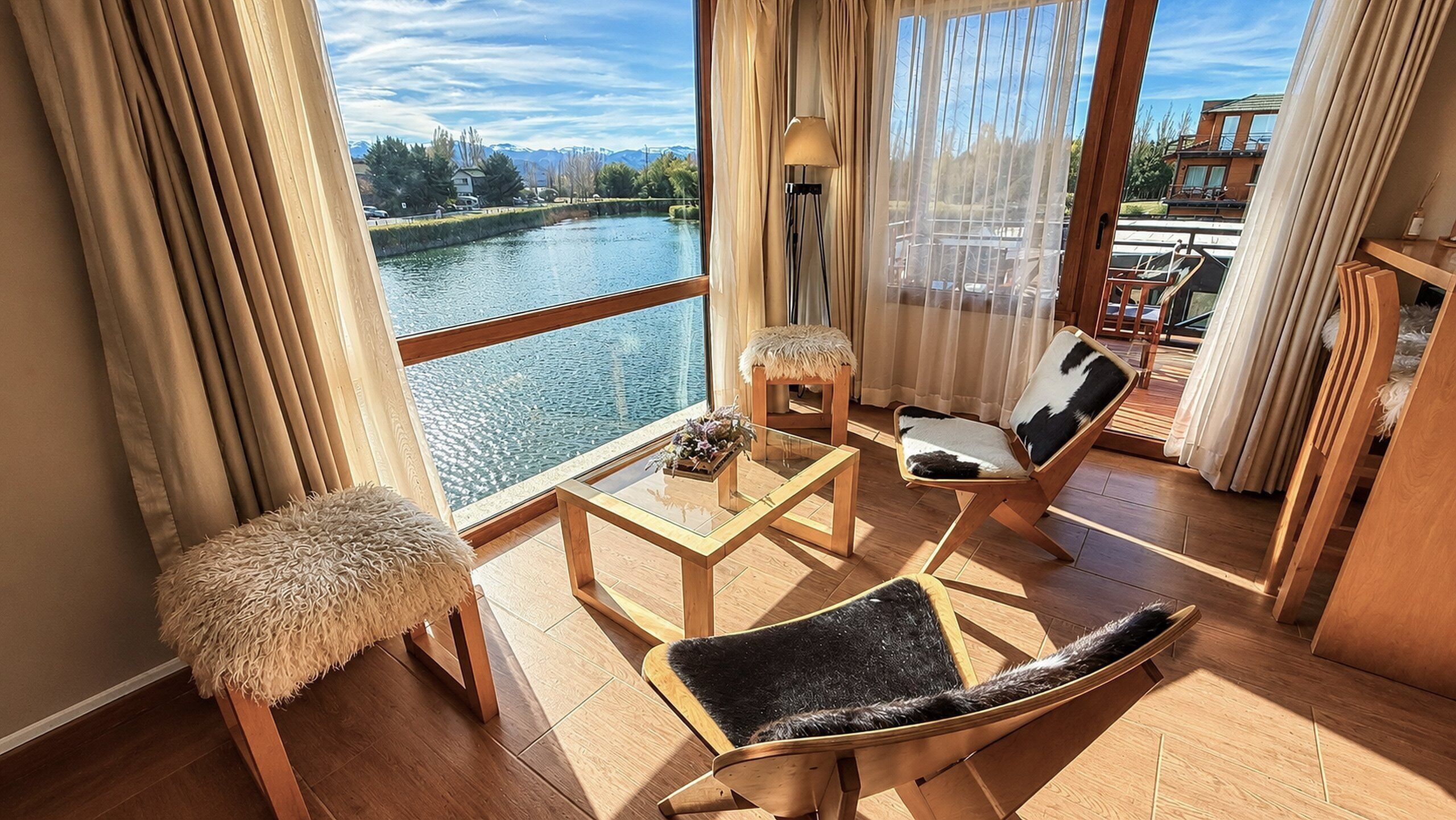 Un balcon donnant sur une rivière, des meubles en bois et une petite table avec une lampe.