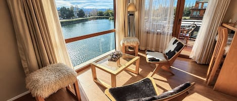 Un balcón con vista a un río, muebles de madera y una pequeña mesa con una lámpara.
