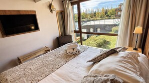 Une chambre d’hôtel dotée d’un grand lit, d’un téléviseur à écran plat fixé au mur et offrant une vue sur un espace paysager aménagé à l’extérieur.