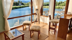 Una habitación con un gran ventanal con vista a un río, dos sillones con cojines mullidos, una mesita y una lámpara.