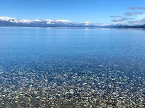 Un lago cristalino con orilla pedregosa y montañas nevadas al fondo.