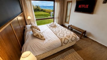 A hotel room with a bed, a bench, a TV, and a view of the outdoors.