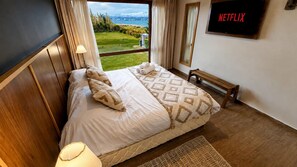 A hotel room with a bed, a bench, a TV, and a view of the outdoors.