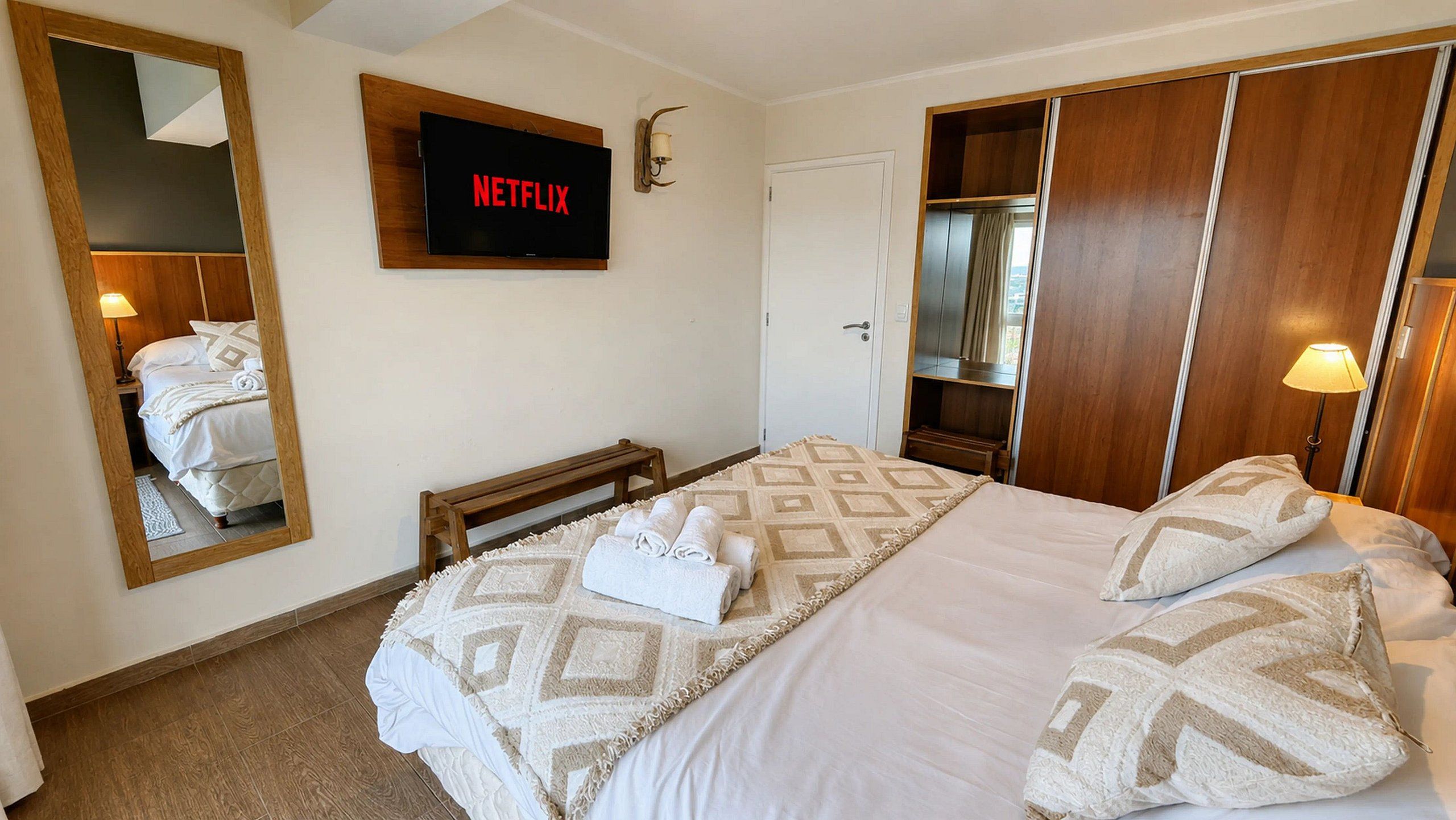 Une chambre d’hôtel comprenant un lit, un téléviseur fixé au mur, une armoire et un miroir.