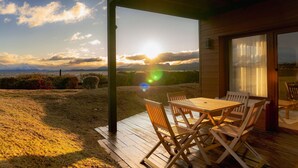 Una terraza de madera con una mesa y sillas, con vistas a un paisaje pintoresco al atardecer.