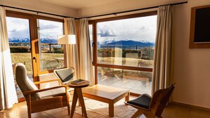 Habitación con un amplio ventanal que ofrece vistas a la montaña, una mesa de madera, dos sillas y una lámpara.