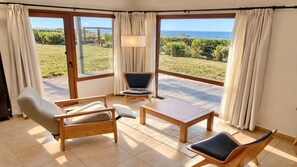 A room with a large sliding glass door leading to a patio with a view of the sea. There are two wooden chairs and a small table. - Garden Superior Moreno Ground Floor Lake Front (Dina Huapi)