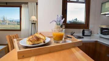 A breakfast tray with croissants and orange juice on a wooden table in a kitchen with a window view.