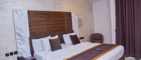 A hotel room with a large bed, a wooden headboard, a nightstand, and a chair.
