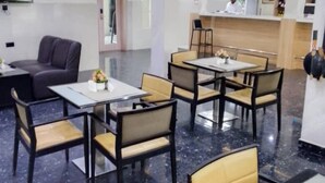 A hotel lobby with a reception desk, seating area with tables and chairs, and a television mounted on the wall.
