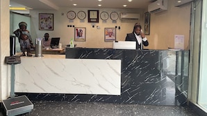 A hotel reception area with a marble reception desk, clocks displaying Dubai, China, Lagos, and New York, and a portrait of a man.