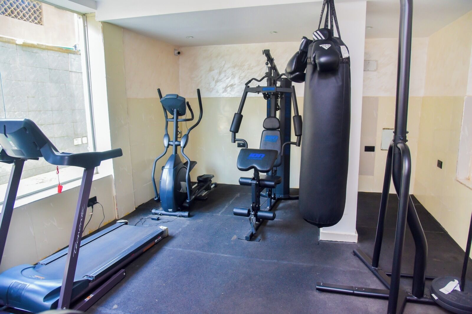 Un gimnasio con cinta de correr, elíptica, máquina de pesas y saco de boxeo.