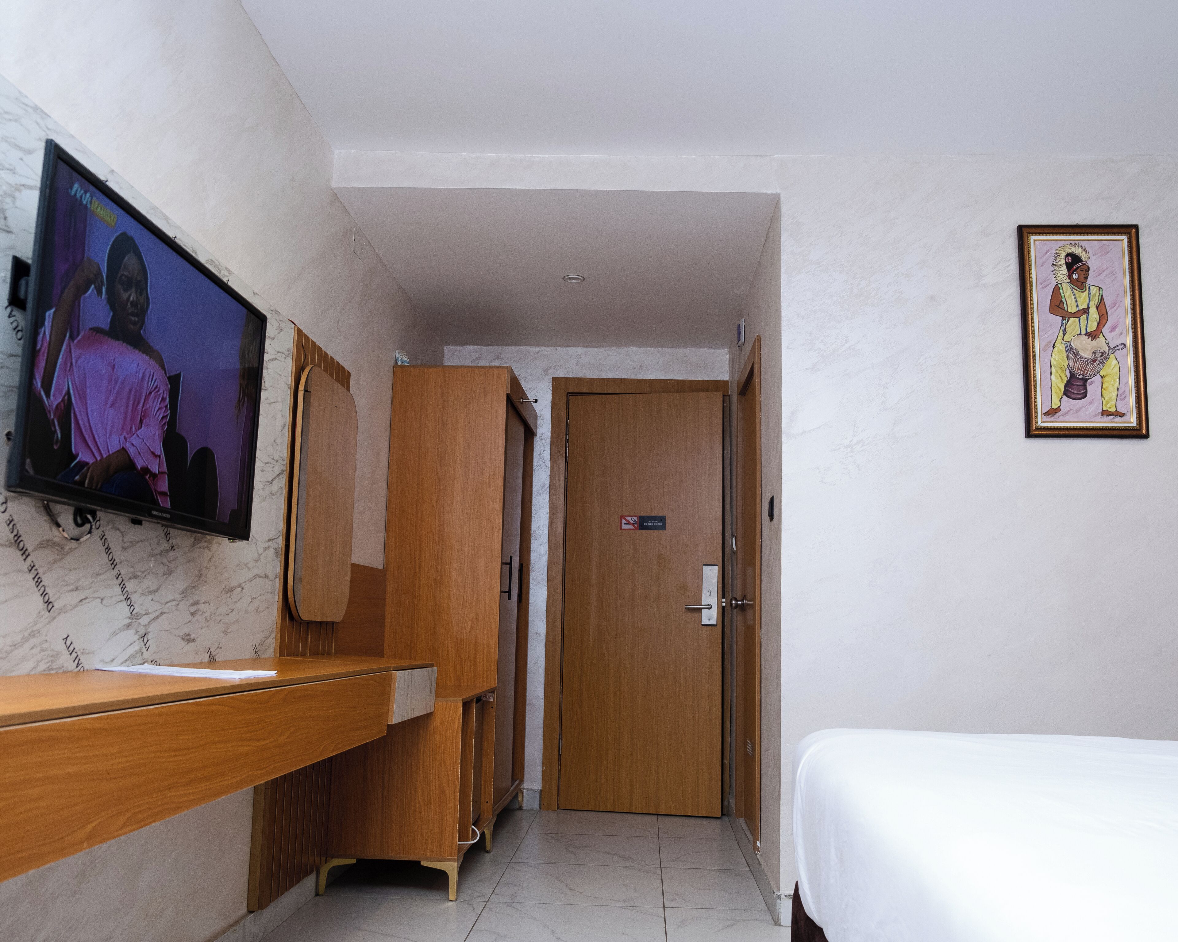 Quarto de hotel com escrivaninha de madeira, televisão na parede, cama e porta.