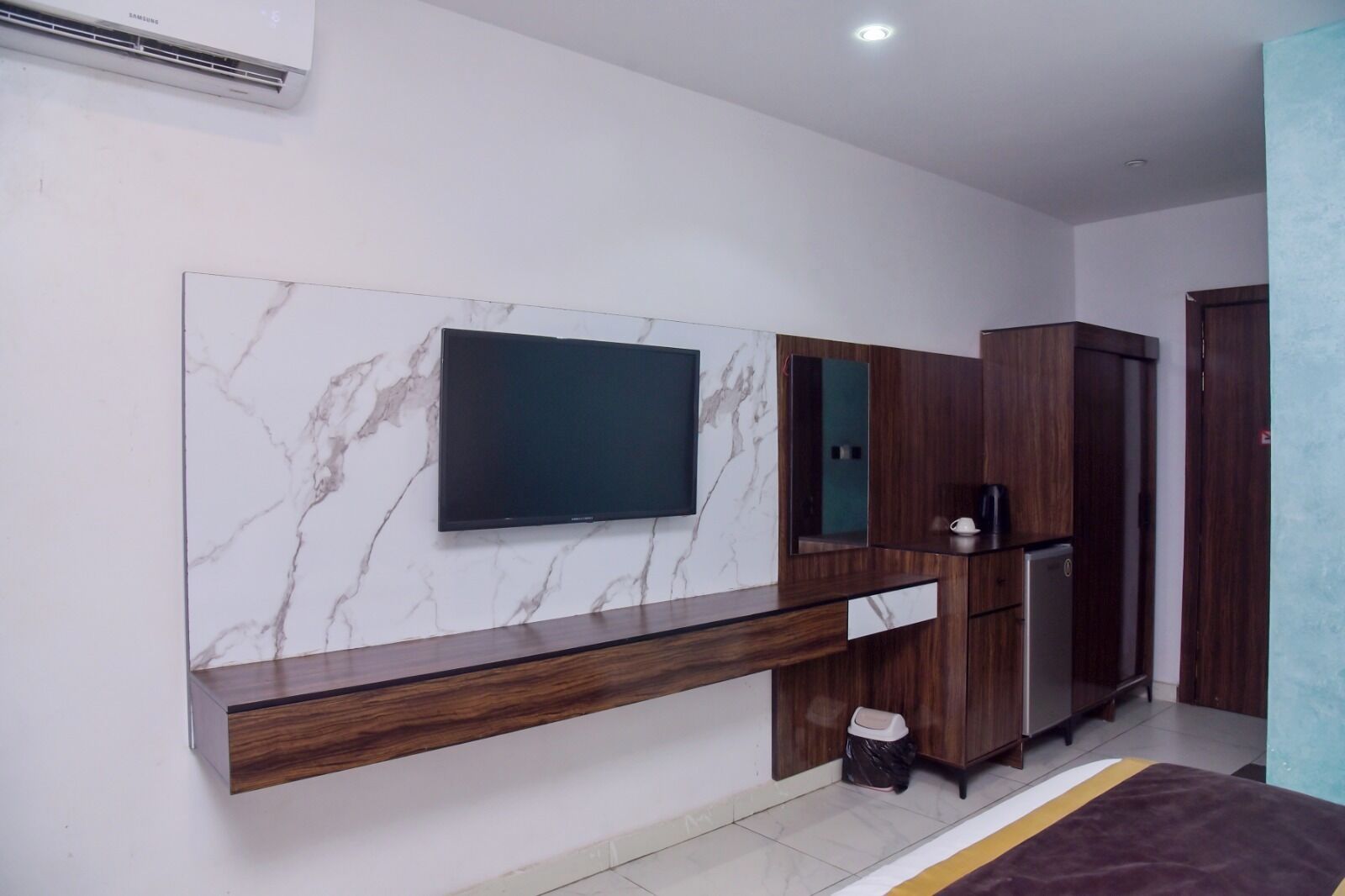 Una sala de estar moderna con un televisor de pantalla plana montado en una pared de mármol, armarios de madera, una cafetera empotrada y un cesto de basura.