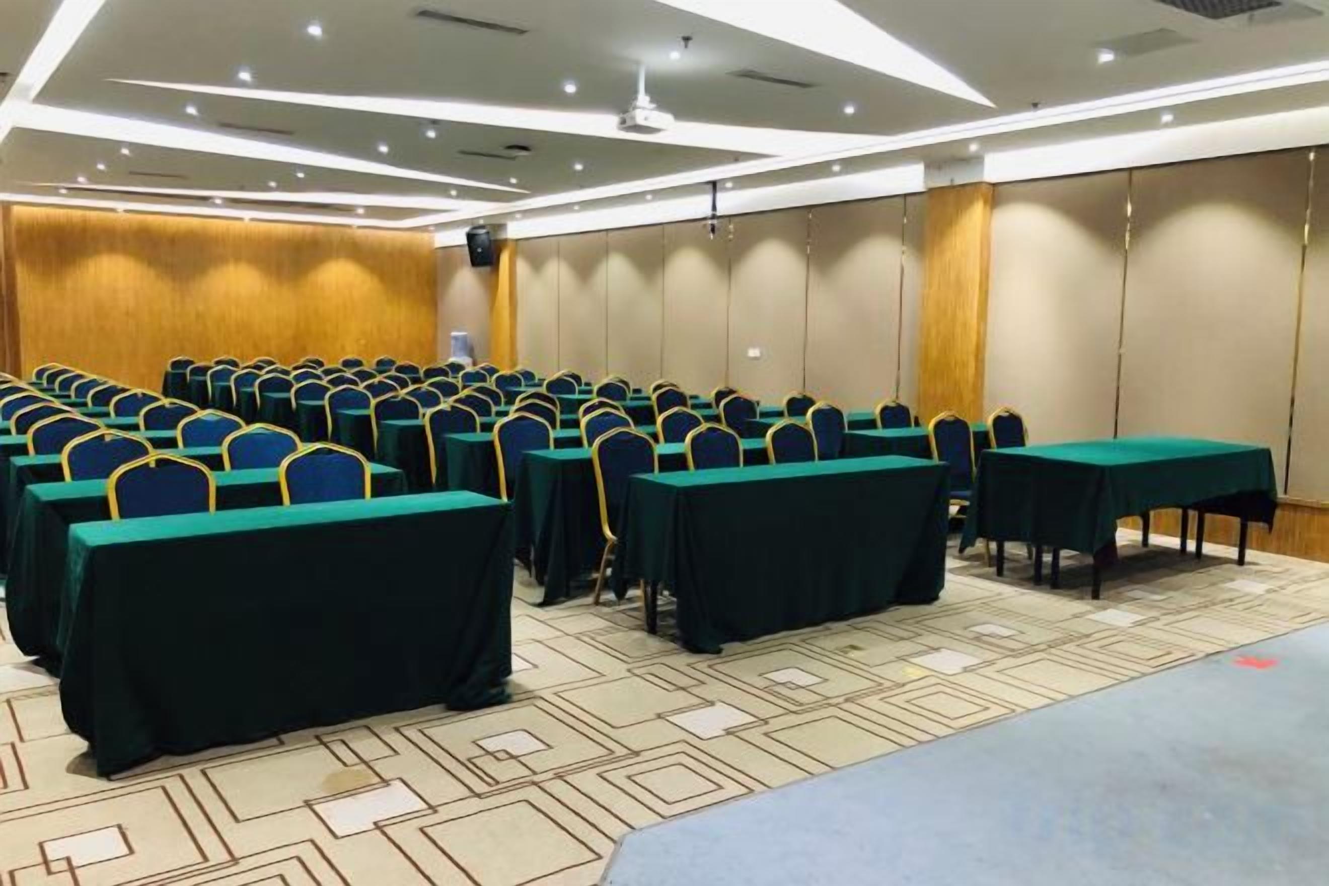 Une salle de conférence avec des rangées de tables et de chaises, un pupitre et un sol recouvert de moquette.