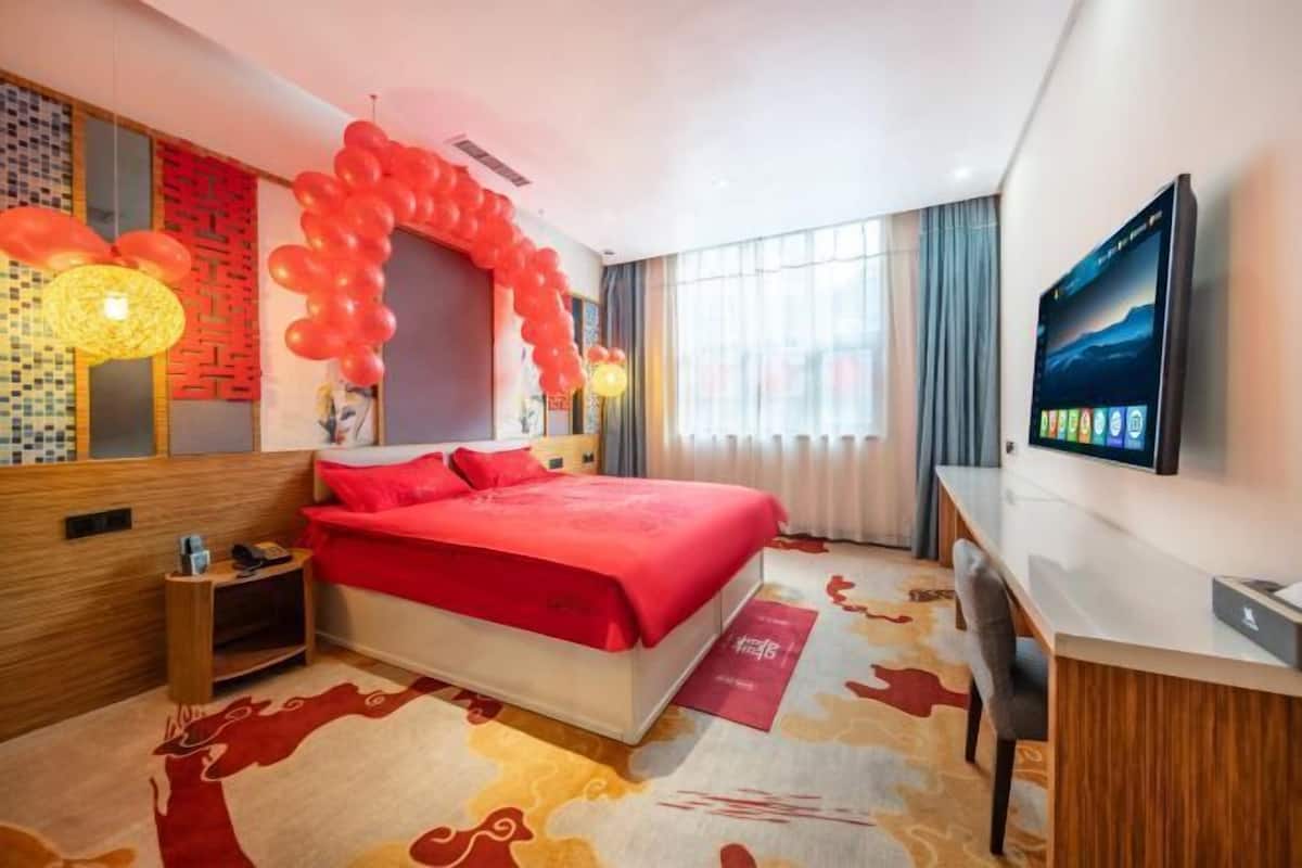 Una habitación de hotel moderna con una cama grande, un escritorio, un televisor y un arco decorativo de globos.