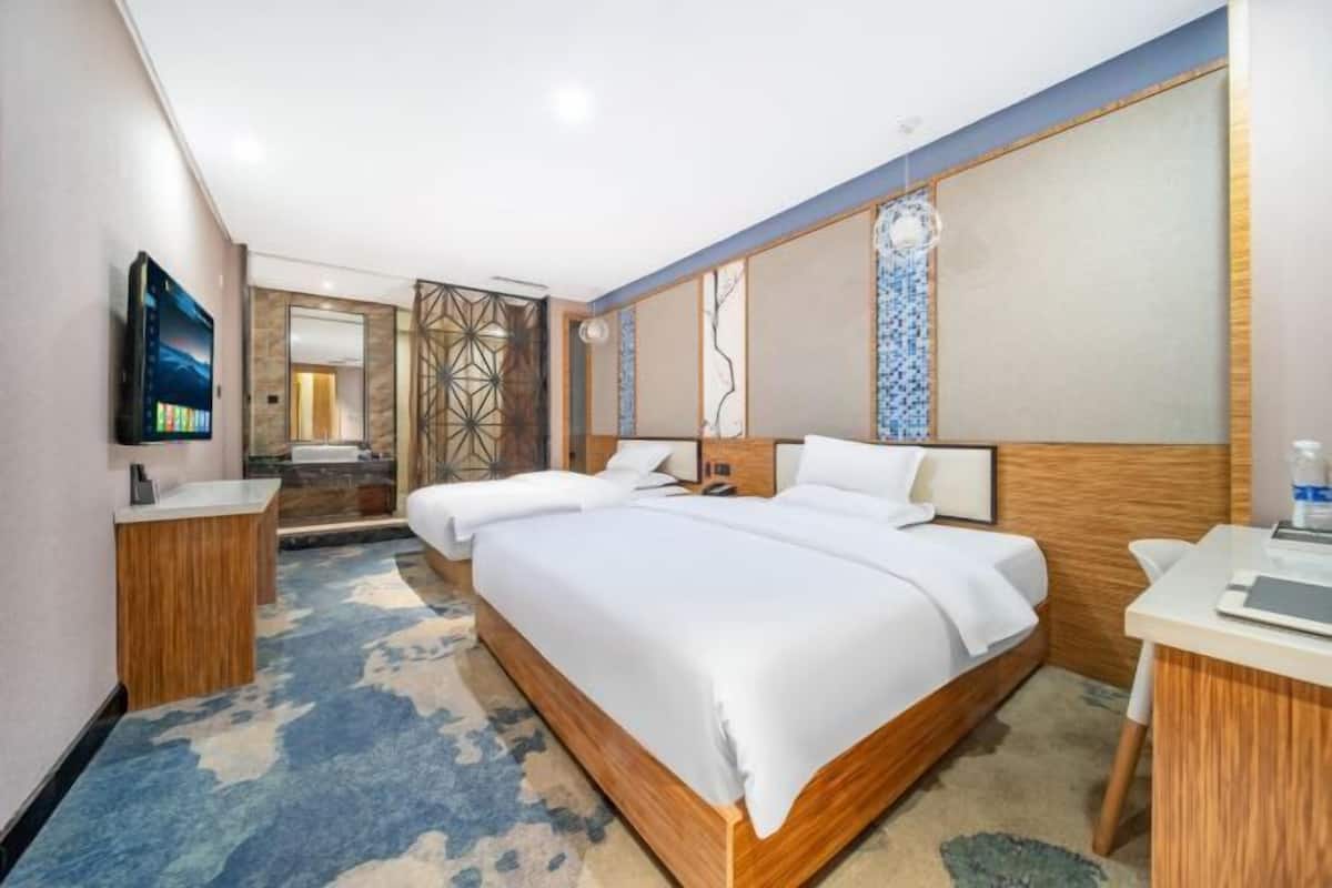 Habitación de hotel con una cama grande, un escritorio, un televisor y un baño con espejo y lavamanos.