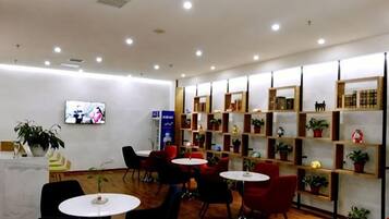Un hall de hotel con arreglos de asientos, una recepción y un televisor en la pared.