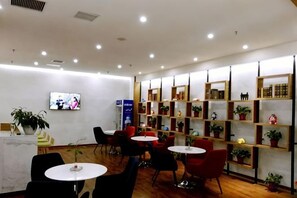 A hotel lobby with seating arrangements, a reception desk, and a wall-mounted television.