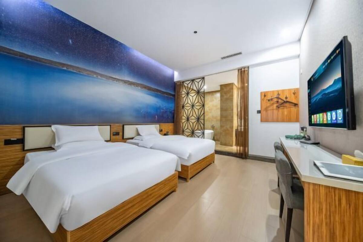 Habitación de hotel con dos camas, un escritorio, un televisor y un mural grande en la pared.