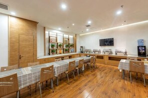 Un comedor con una mesa larga, sillas, un mostrador de buffet y un televisor en la pared.