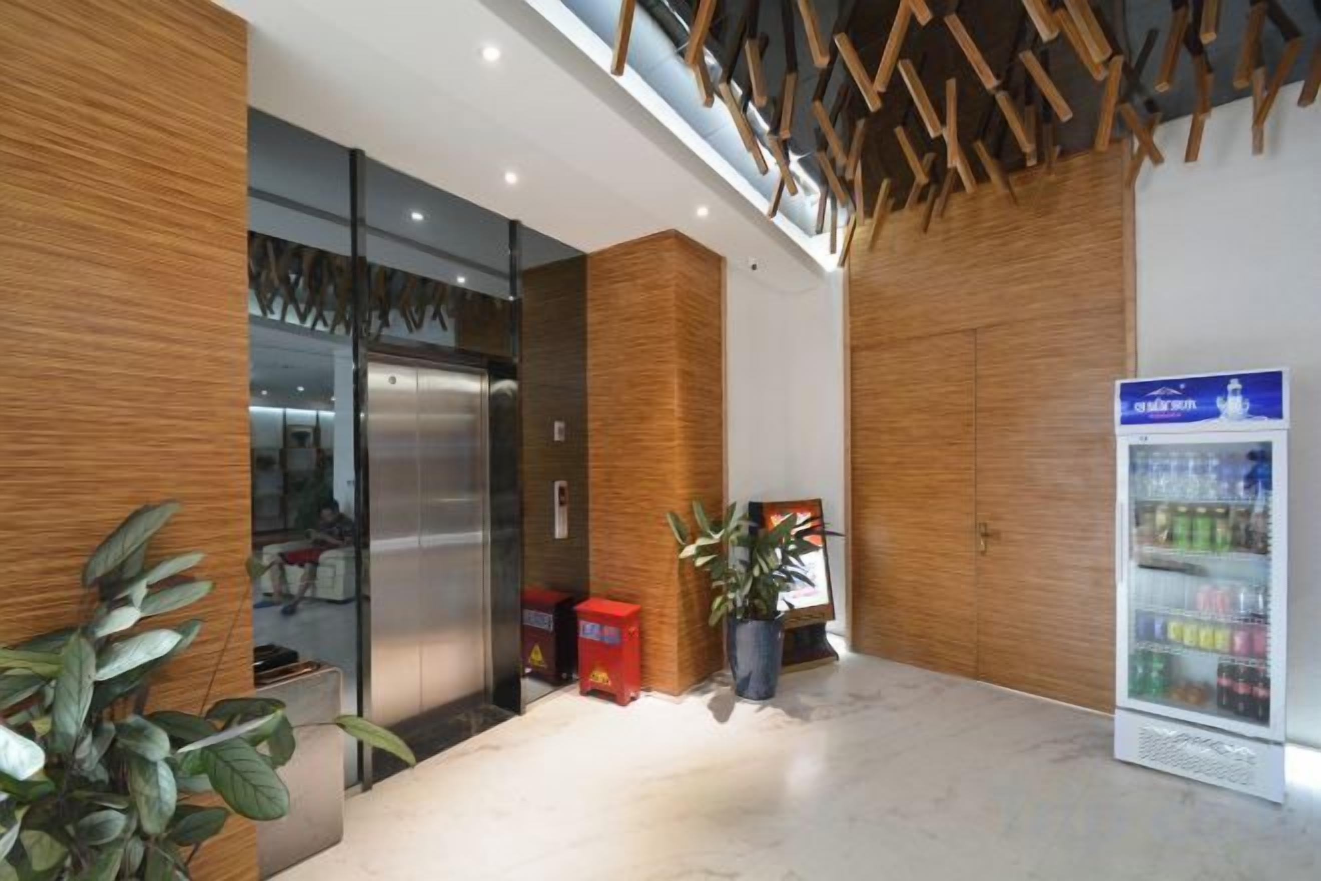 Un área de recepción con diseño moderno, que incluye un mostrador de recepción, un refrigerador y una planta en maceta.