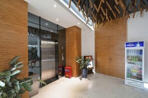 A reception area with a modern design, featuring a reception desk, a refrigerator, and a potted plant. - Aifeier Shishang Hotel (Zhengzhou)