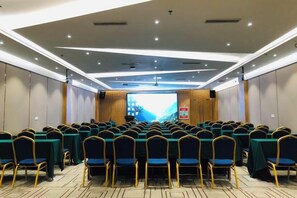 Un salón de conferencias con filas de mesas y sillas, una pantalla grande al frente y un revestimiento de paneles de madera.