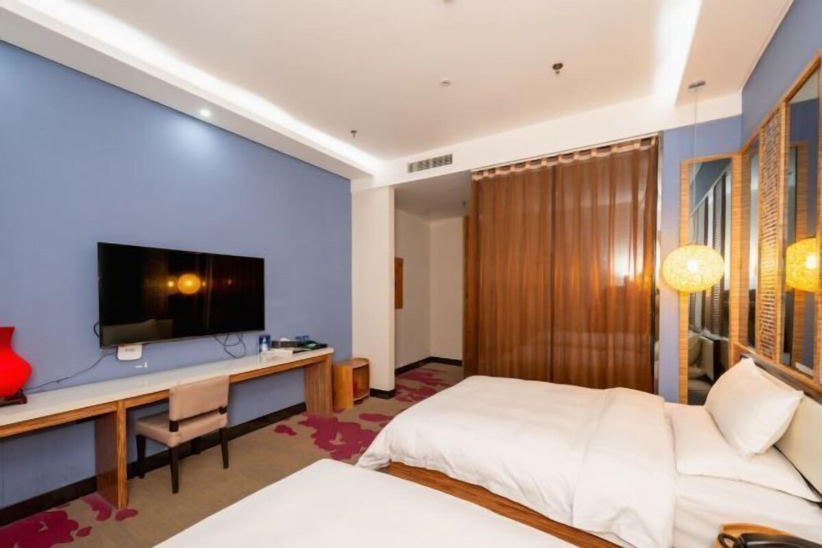 Una habitación de hotel con una cama, un escritorio con silla, un televisor y un espejo grande.