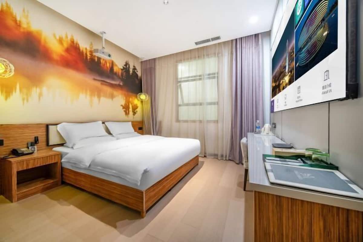 Habitación de hotel con cama, mesita de noche, lámpara y un ventanal con cortinas.