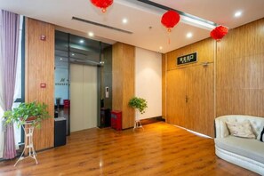 A hotel reception area with a wooden floor, a reception desk, a red sign, and a sofa. - Aifeier Shishang Hotel (Zhengzhou)