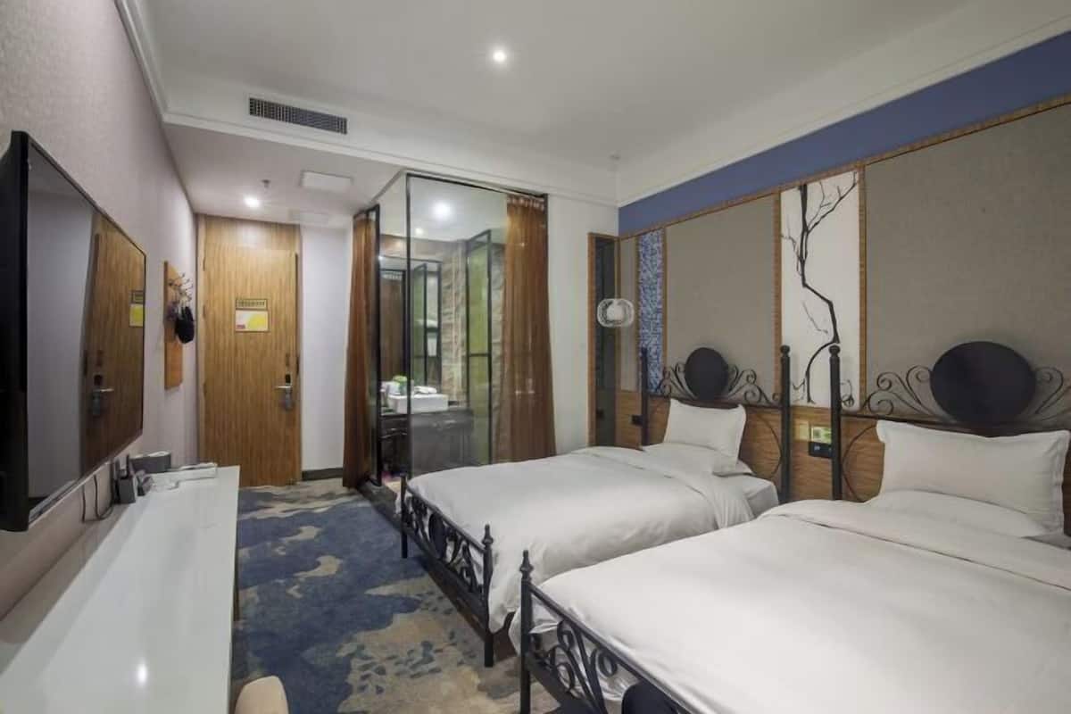 Habitación de hotel con dos camas, un escritorio, un espejo y una puerta corredera hacia el baño.
