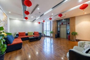 A spacious lobby with a wooden floor, a sectional sofa, and red hanging decorations. - Aifeier Shishang Hotel (Zhengzhou)