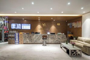 Un espace d’accueil comprenant un comptoir de réception en bois, un écran numérique, un coin salon et un canapé.
