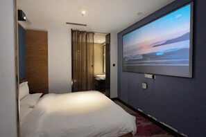 Habitación de hotel con cama, una pantalla grande en la pared y un baño visible a través de una puerta.