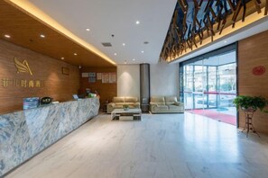 A hotel lobby with a reception desk, seating area, and large windows.