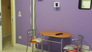 Une pièce aux murs violets, une chaise en métal avec un coussin, une petite table et une porte donnant sur une autre pièce.