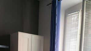 Une chambre à coucher comprenant un lit, une armoire, un radiateur et une fenêtre avec des stores.